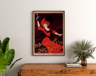 Vintage-Werbeplakat „Absinthe Ducros“ gerahmt über einer Holzkommode, umgeben von Pflanzen.