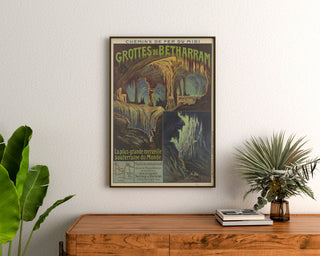 Vintage-Poster Grottes de Bétharram, gerahmt über einer hölzernen Kommode, zwischen Pflanzen.